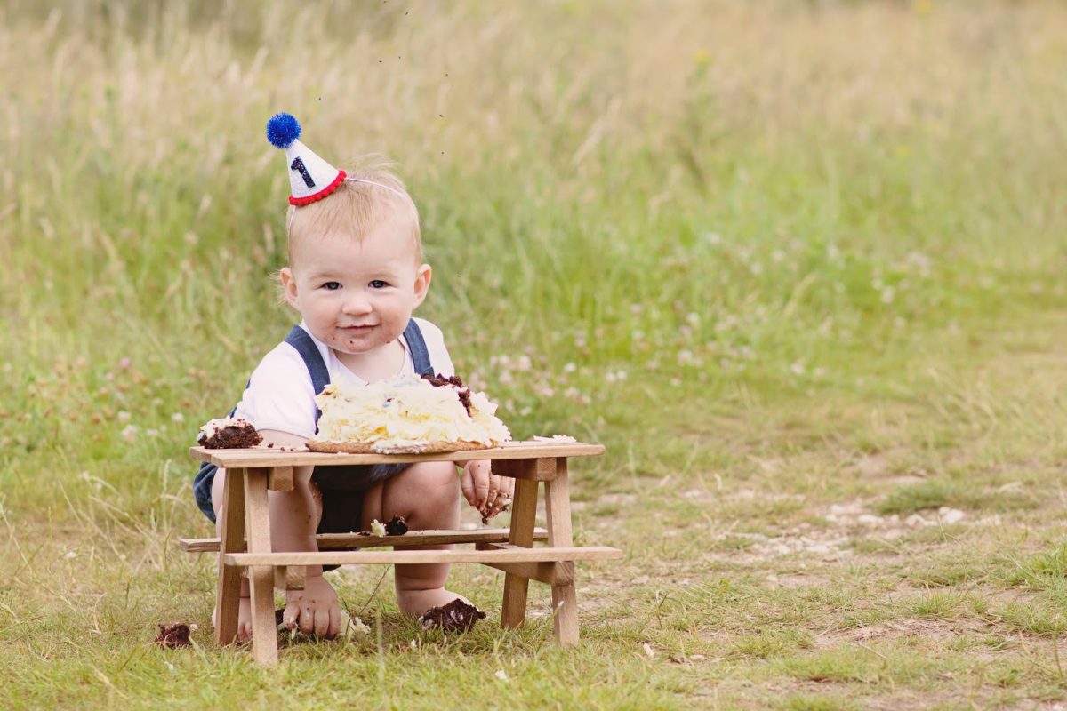 Baby Hero smashing his first birthday cake in a meadow