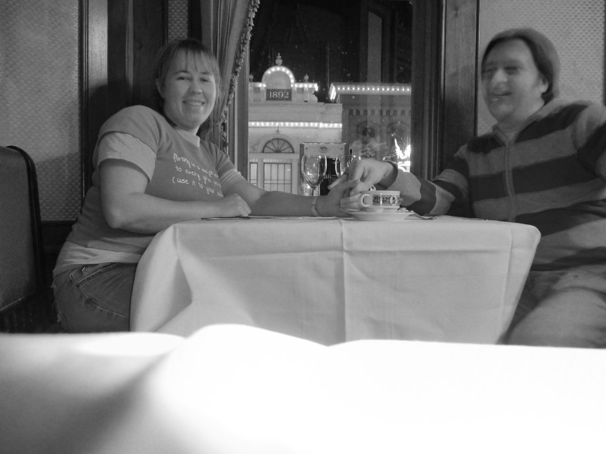Image is a black and white photograph of a couple seated at walt's restaurant on the upper level in disneyland paris at night.