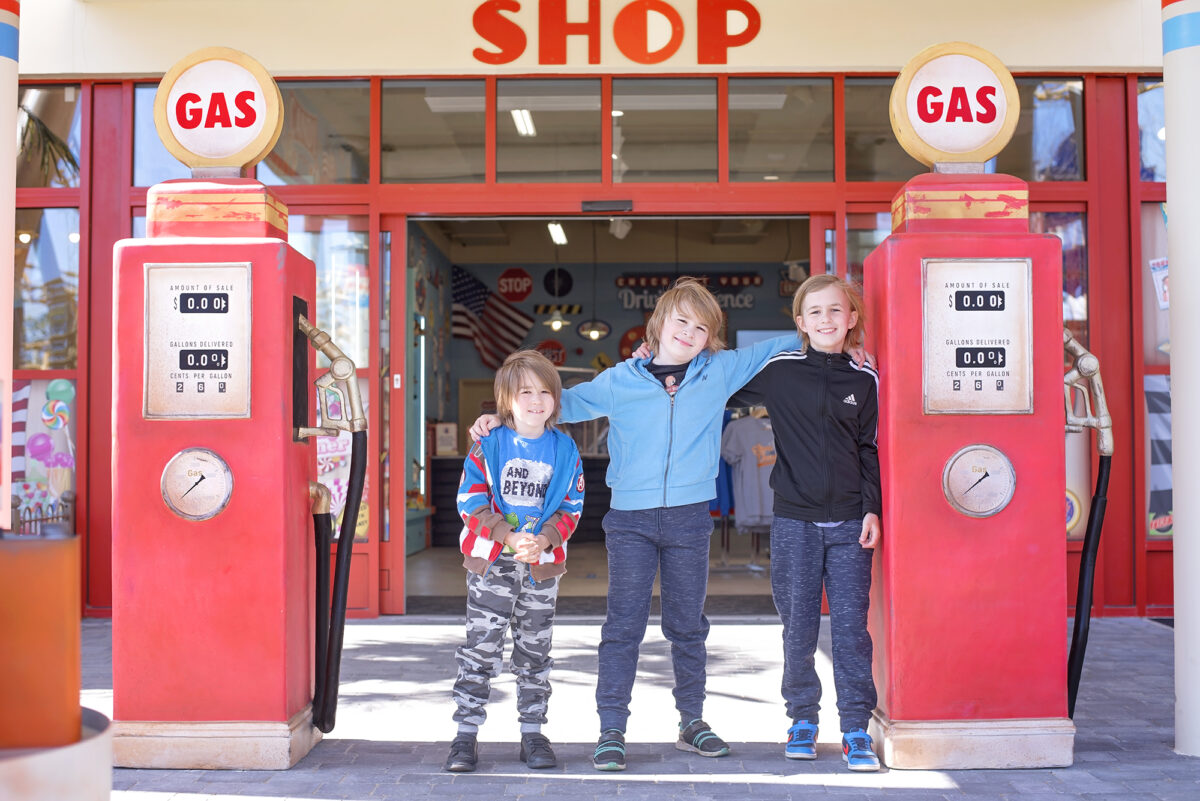 Image shows three boys from Keep Up With The Jones Family stood side by side between the themed entrance to Al's Shop in tornado springs at Paulton's Park in ower, Hampshire. There are two replica red retro gas pumps on either side of the boys.