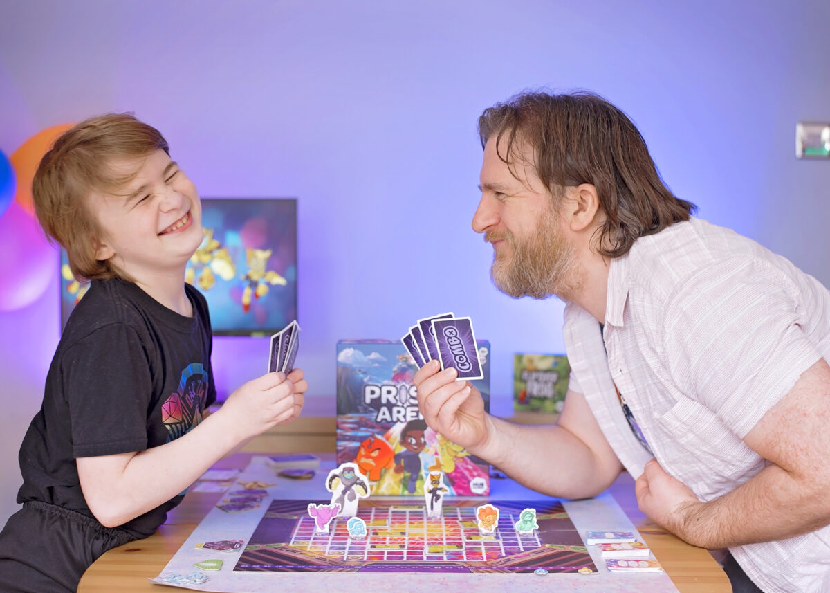 Photo shows father and son laughing whilst playing Prisma Arena from Hub Games. Board Game Geek.