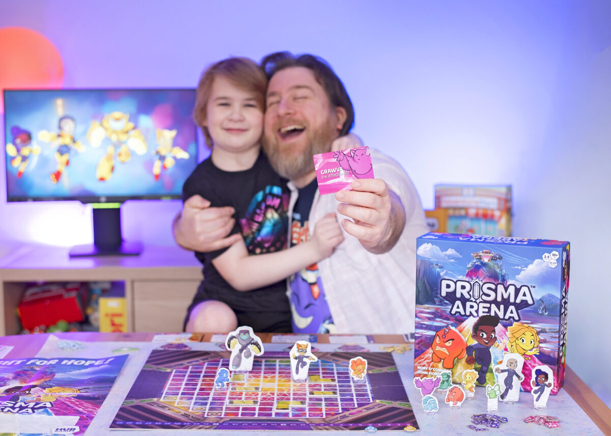 Prisma Arena Mo'kon Grawva brings grappling and hugs into the game from Hub Games. Photo shows Dad and Son hugging whilst holding out the Grawva card from the game.