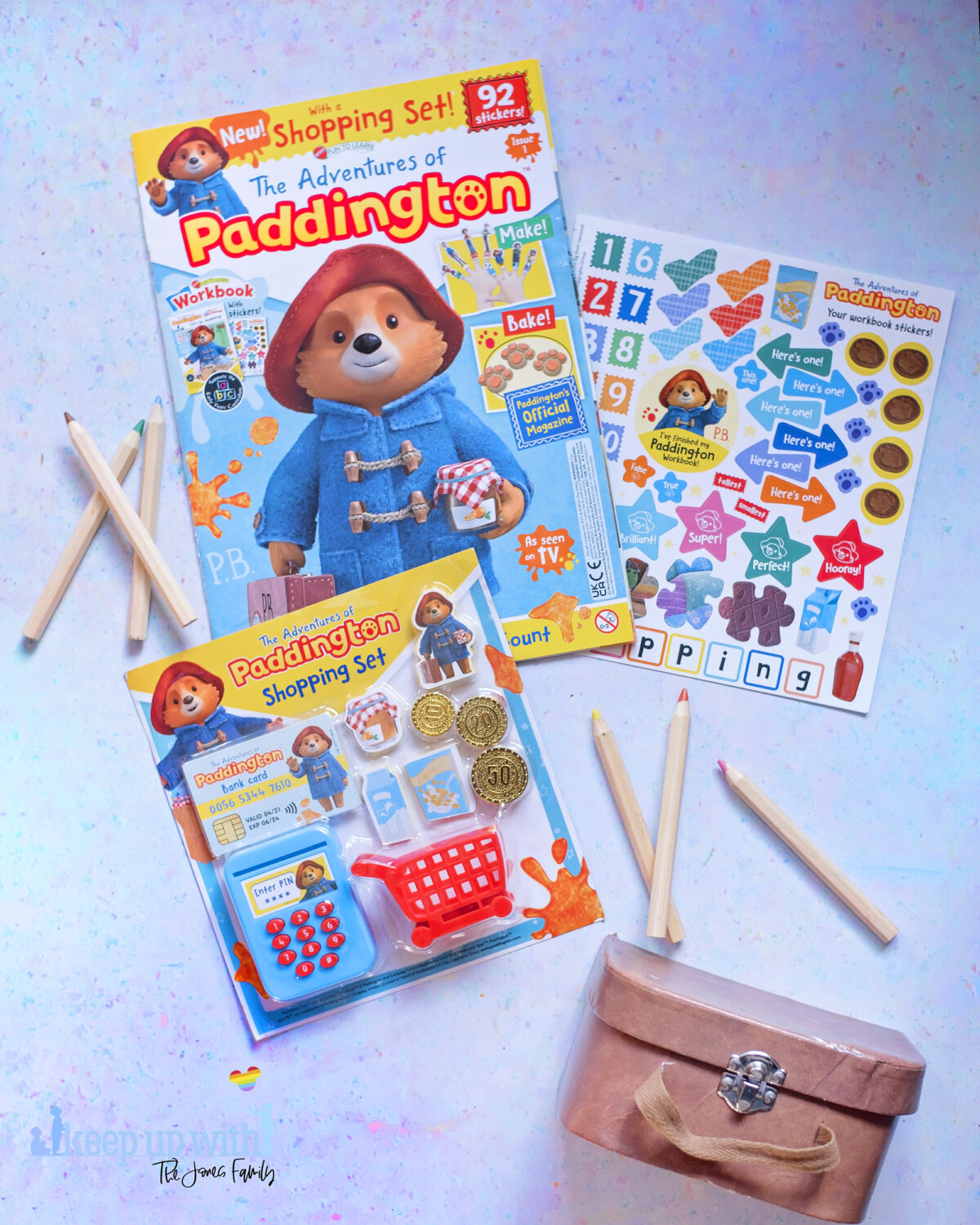The Adventures of Paddington Bear Magazine EYFS. Picture shows issue one with free Paddington Shopping set laid out on blue background. Paddington's brown case is in the photograph. 