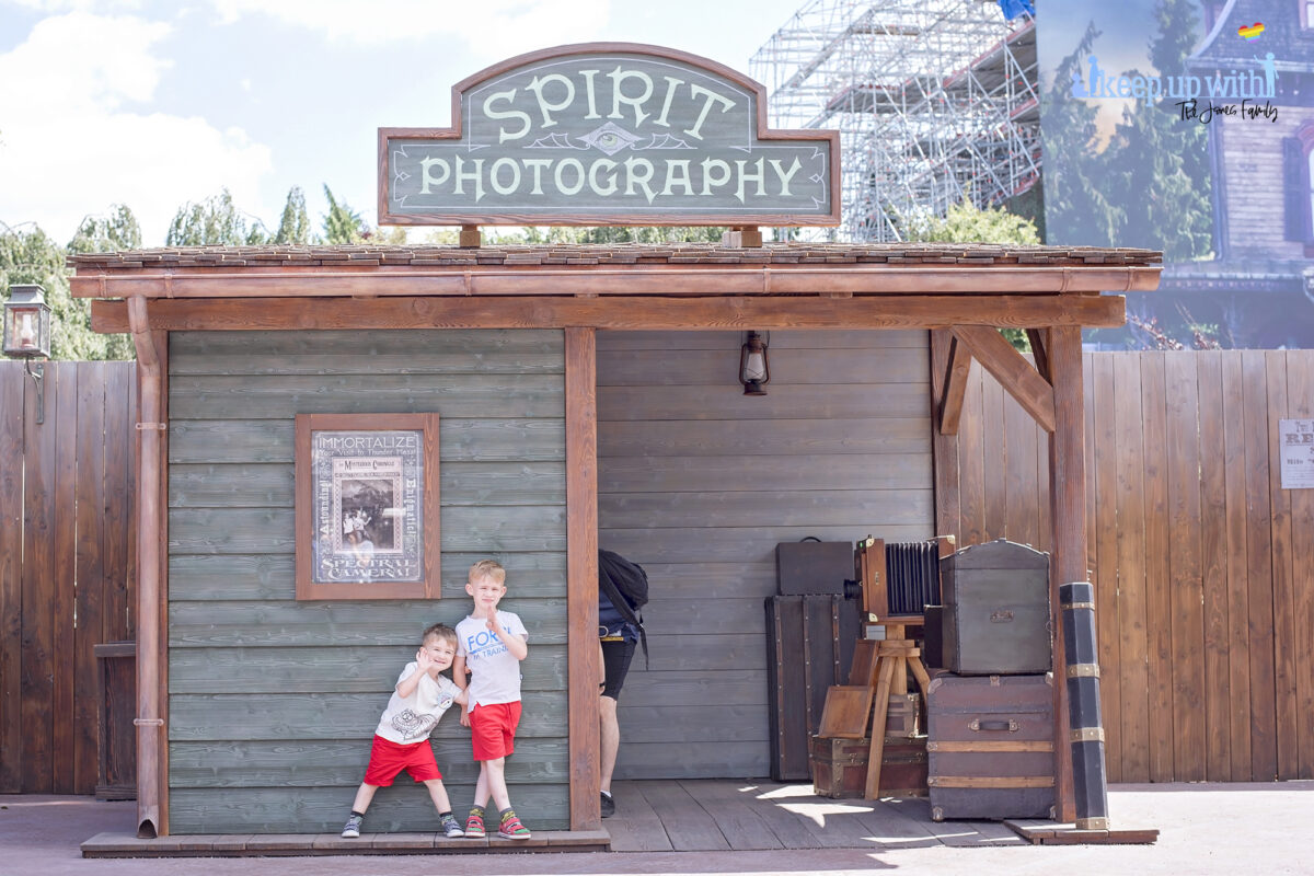 Image shows the Disneyland Paris Spirit Photography Booth in Frontierland and two little boys from the Jones Family dressed in red shorts stood outside smiling.  Image by Keep Up With the Jones Family.
