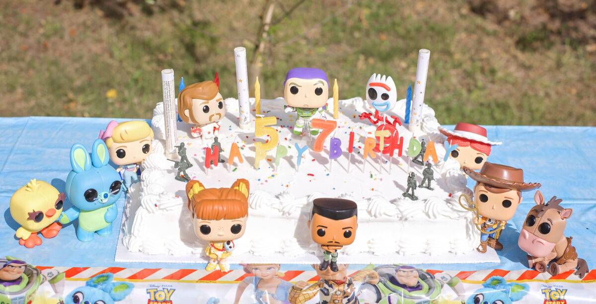 Image shows a semi birds eye view, angled to see the top of a large white Costco cake covered in Toy Story 4 Pop Funko toys.  Combat Carl, Woody, Bullseye, Gabby, Bunny and Ducky, Buzz, Jessie, Forky and Duke kaboom can be seen. 