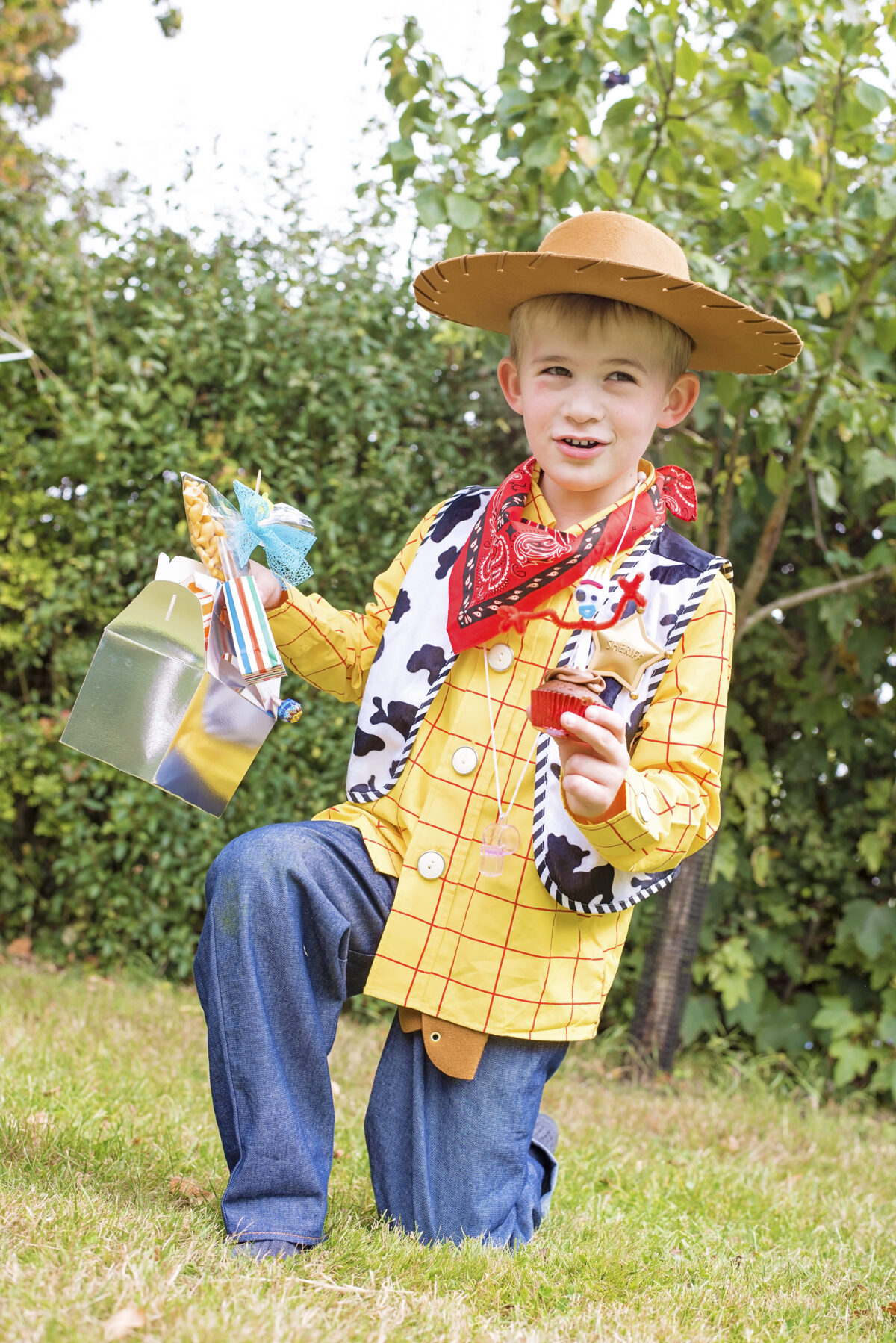 Image shows a member of the Jones Famiily dressed as Woody from Disney's Toy Story and holding a Forky cupcake in one hand and a lunchbox themed for Office Giggles McDimples in the other hand.