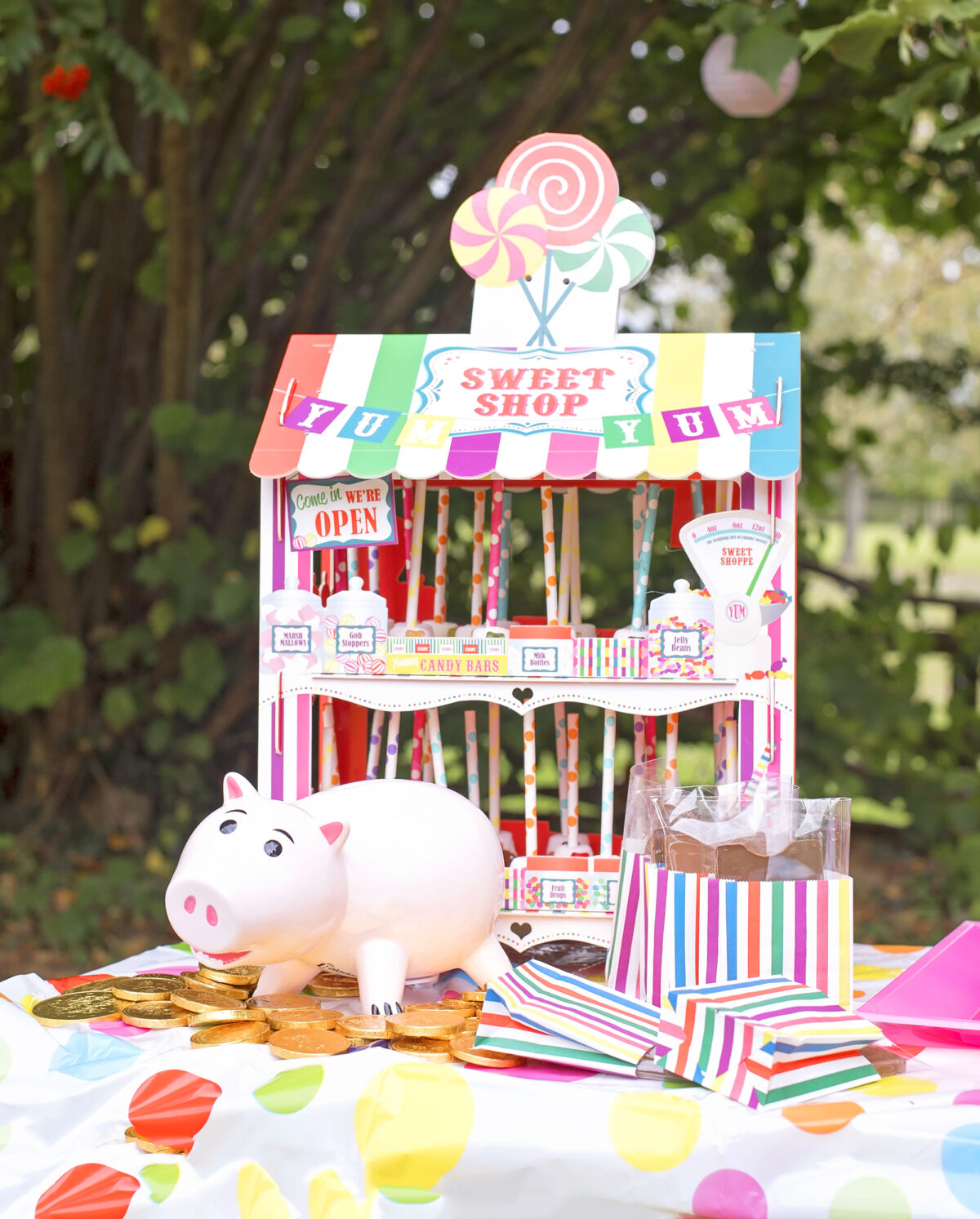 Image shows a ceramic piggy bank in the shame of Hamm from Disney's Toy Story sat on top of a mountain of gold chocolate coins. In the background is a novelty sweet stand filled with chocolate dipped marshmallow pops and in the foreground are chocolate carnival tickets.