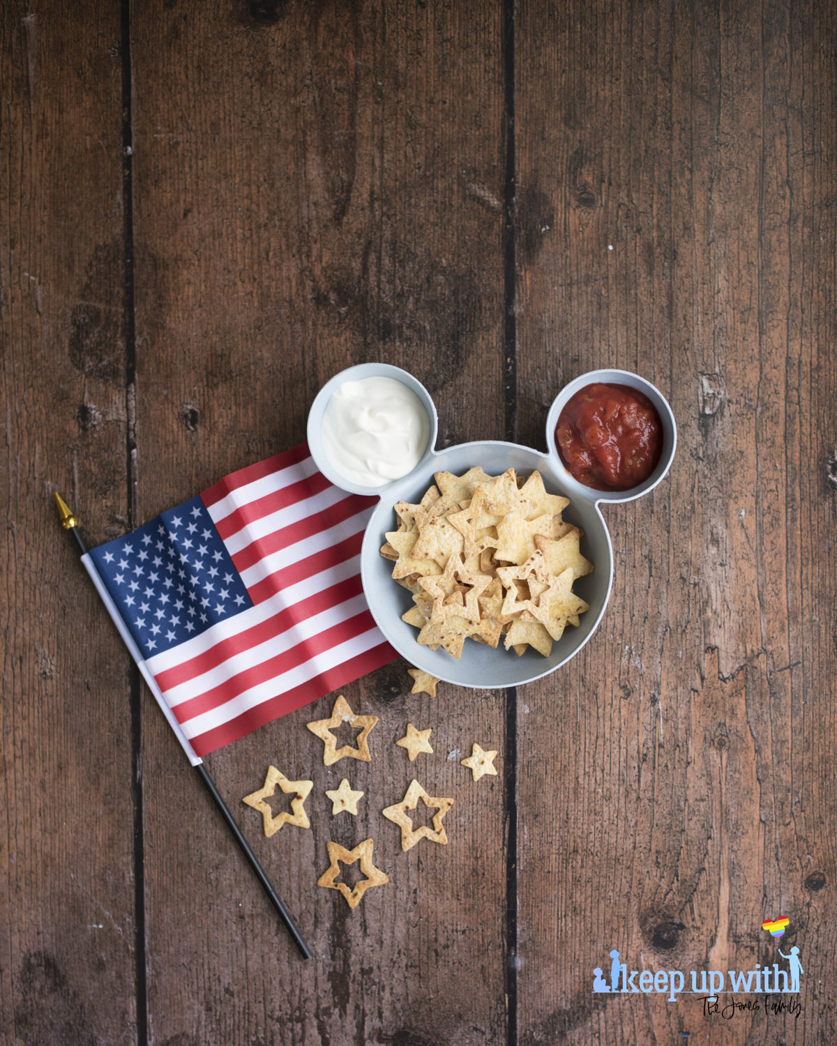 Image shows a blue bowl in the shape of Mickey Mouse suitable for chips 'n' dip. There is an American flag laid close to the bowl on the dark wooden table.  Inside the bowl is tomato salsa, soured cream, and star spangled nacho chips. Image by keep up with the jones family.
