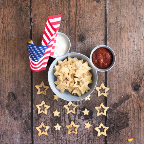 Image shows a blue bowl in the shape of Mickey Mouse suitable for chips and dip. There is an American flag stood close to the bowl and inside the bowl is tomato salsa, soured cream, and star spangled nacho chips. Image by keep up with the jones family.