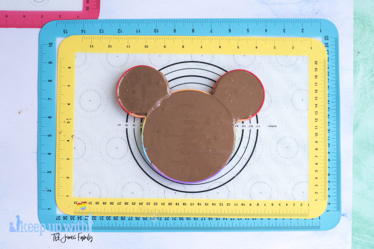 Image shows a rainbow coloured mickey mouse shaped pop-it toy filled with melted chocolate, ready to make a mickey mouse chocolate pop-it bar. Image by keep up with the jones family.