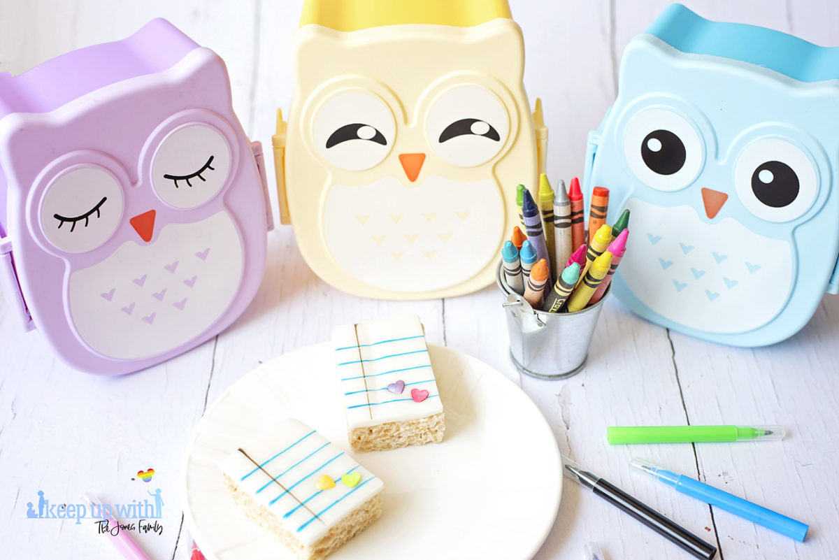 Image shows Back to School Rice Krispie treats on a white Vera Wang for Wedgwood plate. There are three pastel coloured owl bento boxes in the background and a small tin bucket of Crayola crayons alongside it. Cake pens surround the plate on the white wooden background. Image by Sara-Jayne from Keep Up With The Jones Family.
