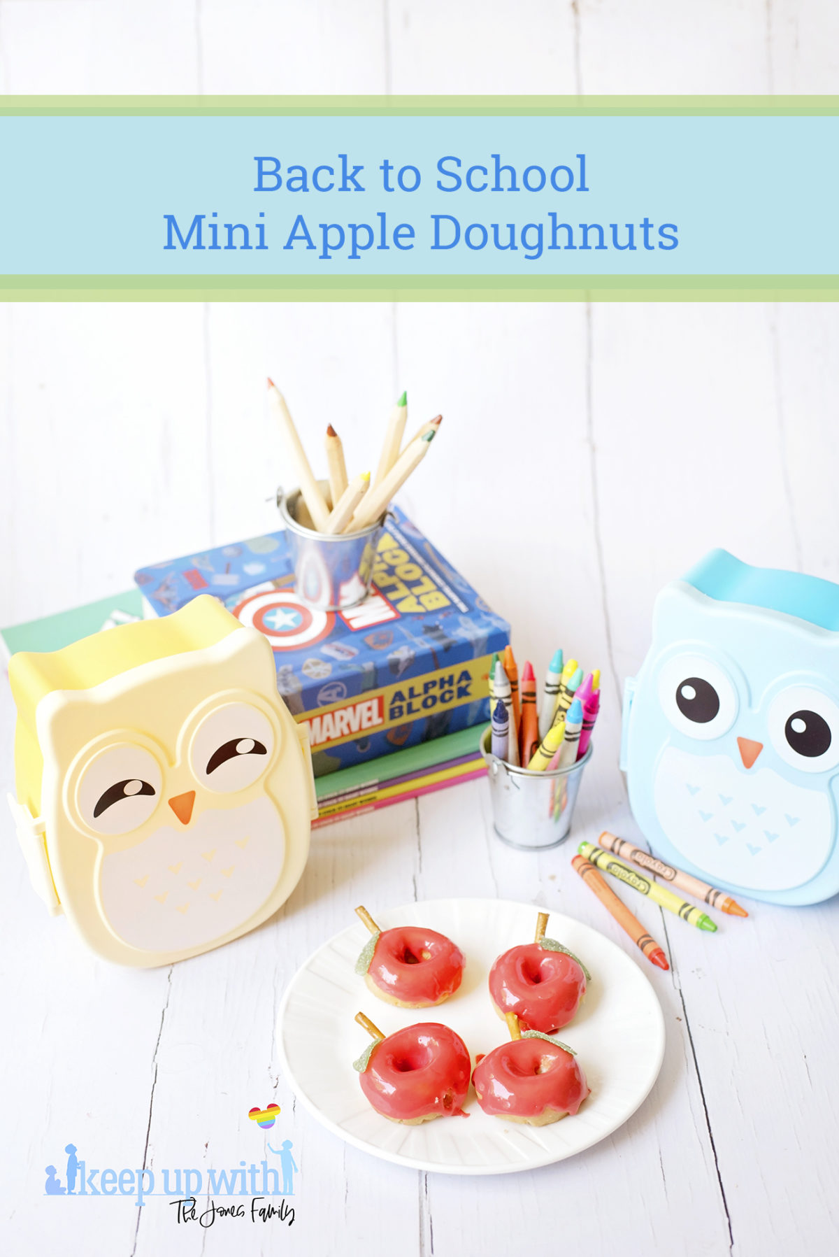 Image shows red apple shaped Back to School Doughnuts on a white Vera Wang plate, sitting on a white wooden surface. There are two small owl shaped bento boxes and books in the background, along with a bucket of crayola crayons. Image by Sara-Jayne from Keep Up With The Jones Family.
