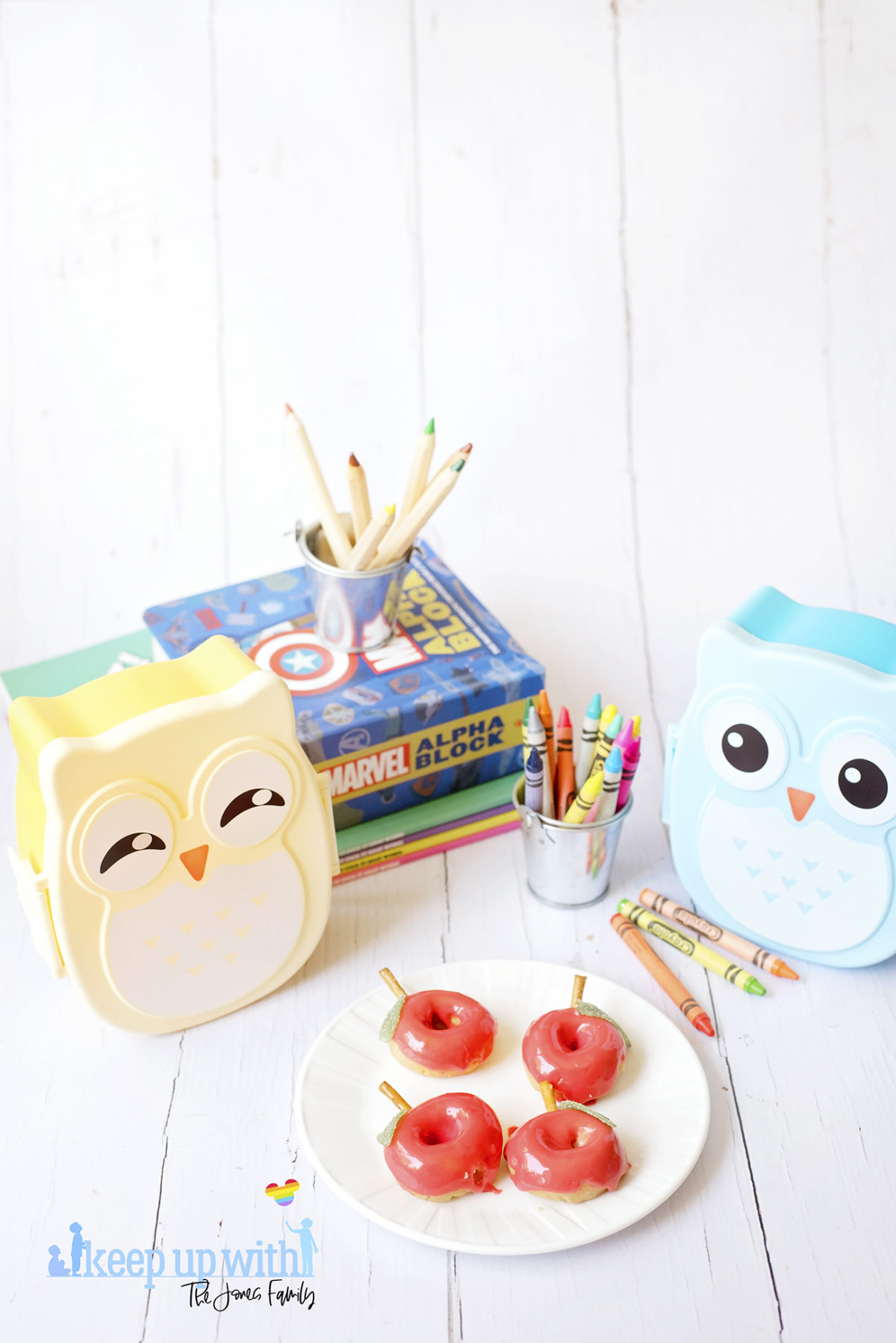 Image shows Back to School Doughnuts on a white Vera Wang plate, sitting on a white wooden surface. There are small owl shaped bento boxes and books in the background, along with a bucket of crayola crayons. Image by Sara-Jayne from Keep Up With The Jones Family.