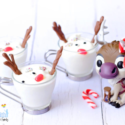 Image shows a Disney's Frozen Sven the Reindeer Funko Pop Vinyl decorated with mini red and white peppermint candy canes on his antlers. The figure is sitting next to three Melted Sven the Reindeer Yoghurts in glass cups with silver handles, on a white wooden tabletop. Image by Keep Up With The Jones Family.